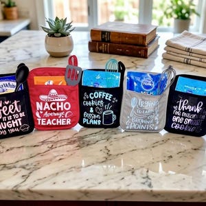 Pode incluir: Cinco pegadores de panela de tecido nas cores preta, vermelha e cinza, cada um com um bolso frontal contendo uma mistura para bolo e um utensílio de cozinha. Os pegadores exibem textos em branco, incluindo frases como How Sweet It Is To Be Taught By You e Nacho Average Teacher.