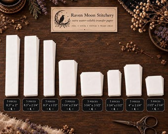 May include: Eight stacks of white water-soluble transfer paper labeled Raven Moon Stitchery. Each stack has five pieces with dimensions ranging from 8.5 by 2 inches to 2.5 by 2.25 inches, displayed with a pair of metal scissors.