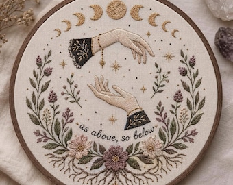 May include: An embroidery hoop featuring a cream fabric background with two hands reaching toward each other. The design includes a moon phase cycle, gold stars, and a floral wreath at the bottom with the text as above, so below.