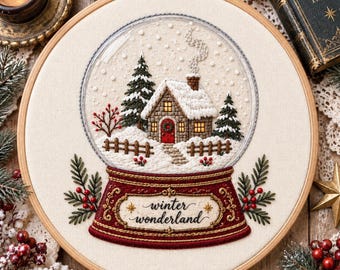 May include: A circular embroidery hoop featuring a snow globe design on cream fabric. Inside the globe is a stone cottage with a red door, snow-covered trees, and a fence. The base is deep red with the text winter wonderland embroidered in gold.