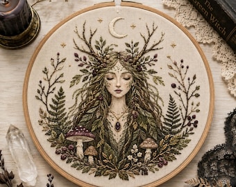 May include: A circular embroidery hoop featuring a detailed thread-stitched portrait of a figure with antlers, surrounded by ferns, leaves, and mushrooms. Above the figure is a crescent moon and stars, with a purple pendant necklace visible.