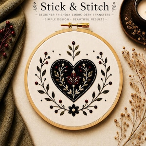 Puede incluir: Un bastidor de bordado redondo de madera que contiene tela blanca con un diseño en forma de corazón negro con bayas rojas y hojas verdes. El texto Stick & Stitch, Beginner Friendly Embroidery Transfers, Simple Design, Beautiful Results es visible.