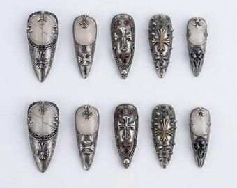 May include: A collection of ten silver-toned nail shields. Each shield features intricate designs, including crosses, skulls, and decorative embellishments. Some have light-colored stone accents. The shields are arranged on a white surface.