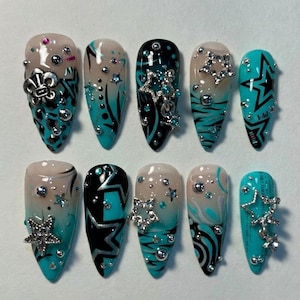 May include: A set of ten long, almond-shaped artificial nails. Each nail features a unique design with a base of teal, black, and white, adorned with silver star and bead embellishments. Some nails have a gradient effect.