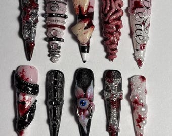 Peut inclure: Un ensemble de dix faux ongles en forme de stylet avec des motifs d'horreur. Les décorations incluent des dents en 3D, un globe oculaire bleu, des éclaboussures de sang rouge, de la dentelle noire, des chaînes argentées, des perles blanches, une croix et le mot Pierce écrit en noir.