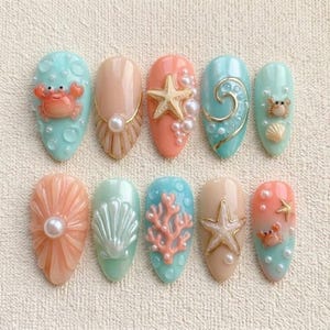May include: A collection of ten artificial nails with a marine theme. The nails showcase designs such as a crab, starfish, coral, and seashells, in shades of blue, peach, and beige. Some nails have pearl accents and gold detailing.