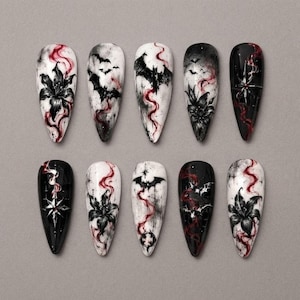 Puede incluir: Un juego de diez uñas postizas en forma de almendra con una estética gótica sobre fondos blancos y negros, ilustraciones detalladas de lirios negros, murciélagos voladores y estrellas, acentuadas con patrones de humo rojo en espiral.