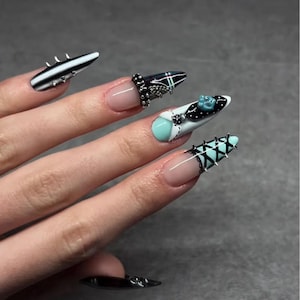 May include: Stiletto-shaped artificial nails featuring a mix of black, white, and mint green colors. The designs include silver metal studs, intricate black lace-up corset patterns, and a small blue decorative accent on one nail surface.