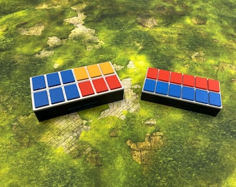 May include: Two rectangular game pieces with colorful blocks. One has blue, yellow, and red blocks, the other has red and blue blocks. The pieces are on a green and yellow patterned surface.