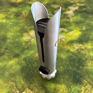 May include: A silver lightsaber hilt with a black accent and a white base. The top of the hilt has a curved design. The text "ROGUE WORK" is visible on the top. The hilt is cylindrical and has a detailed design.