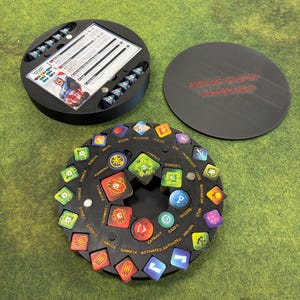 May include: A black board game organiser with a circular design. The organiser includes a lid with the text "ROGUE GROVE WORKSHOP" and a central rotating piece with various game tokens. The tokens are in various colours and shapes.