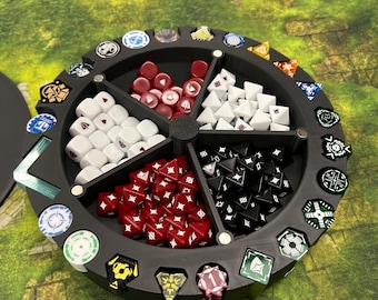 May include: A black, circular dice and token organizer with multiple compartments. The organizer holds various dice in red, white, and black, along with colorful tokens. The organizer sits on a green and brown surface.