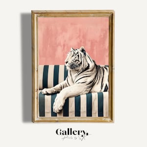 May include: A framed art print featuring a white tiger reclining on a striped blue and white sofa. The background is a textured pink wall. The frame is gold. The print is from Gallery Prints by SK.