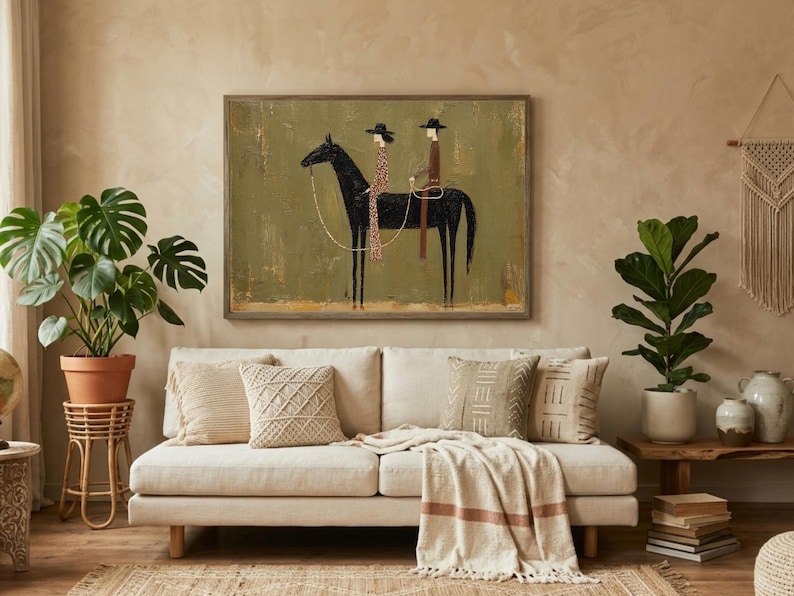 May include: A framed artwork depicts a black horse with two riders in hats. The riders are wearing patterned clothing. The artwork hangs above a cream-colored sofa with decorative pillows and a throw blanket. A potted plant and a side table are also visible.