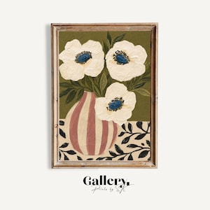 May include: A framed art print depicting white flowers with blue centres in a striped vase. The vase is on a patterned surface, set against a green background. The artwork is signed "Gallery Prints by SK".