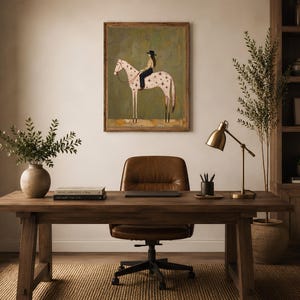 May include: A framed wall art print featuring a stylized illustration of a person wearing a hat riding a white horse with brown star markings against a muted olive green background. The artwork is displayed in a simple wooden frame.