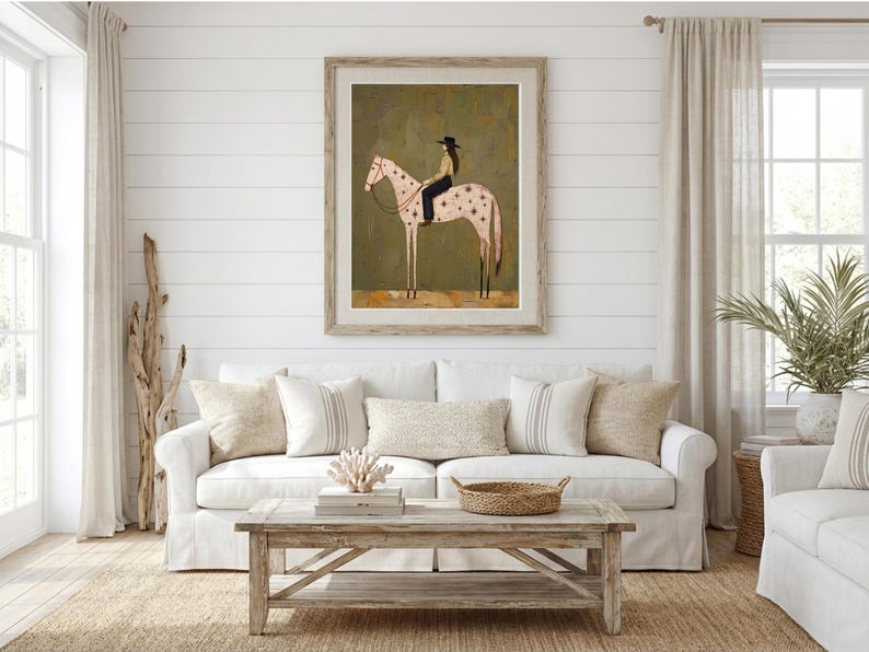 May include: A framed wall art print featuring a stylized illustration of a person wearing a black hat and dark clothing riding a light-colored horse with dark star-shaped markings on its body, set against a muted olive green background.