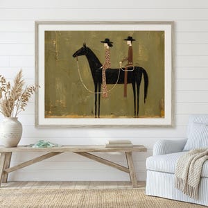 May include: A framed wall art print featuring a stylized black horse with two figures riding on its back. The figures wear hats and long garments, one in a brown tone and the other in a patterned brown. The background is a textured olive green.