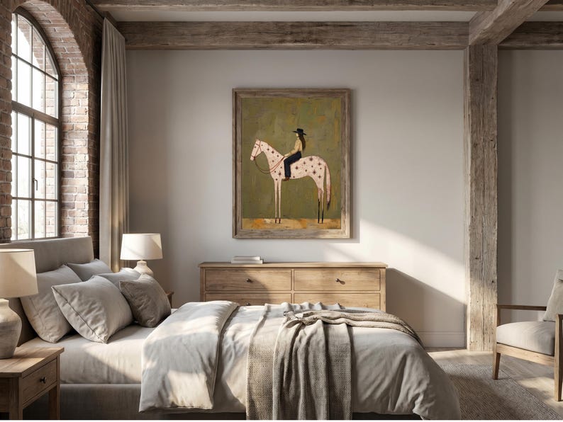 May include: A framed wall art print featuring a stylized illustration of a person wearing a black hat and dark clothing riding a light-colored horse with dark spots. The horse is positioned in profile against a muted olive green background.