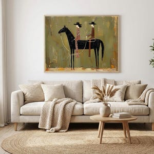 May include: An abstract painting depicts two figures on horseback. The black horse is the focal point, with riders in hats and patterned clothing. The background has a textured, olive-green appearance, and the artwork is framed in a light-colored wooden frame.