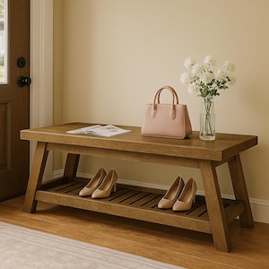 May include: A wooden entryway bench with a lower shelf, holding two pairs of beige high heels. A light pink handbag, a magazine, and a vase of white flowers sit on the bench. The bench is made of light brown wood.