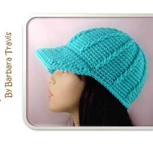 Puede incluir: Un gorro de punto de ganchillo azul turquesa con visera. El gorro tiene un patrón de punto de cable y lo lleva puesto un maniquí.