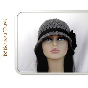 Könnte beinhalten: Ein grauer und schwarzer Häkel-Cloche-Hut mit einer schwarzen Schleife an der Seite. Der Hut sitzt auf einem Mannequin mit langen schwarzen Haaren.