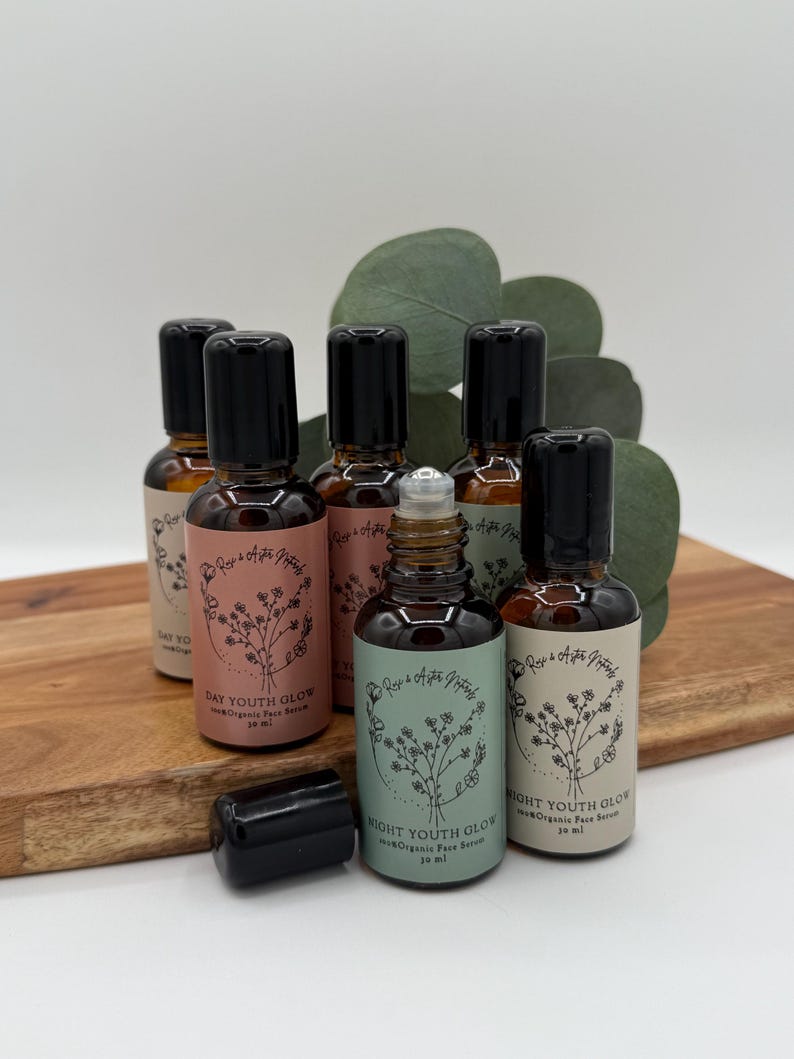 May include: A collection of small, brown glass bottles with black caps, labeled with text and floral designs. The bottles are arranged on a wooden cutting board with green foliage in the background. The labels read "Day Youth Glow" and "Night Youth Glow".