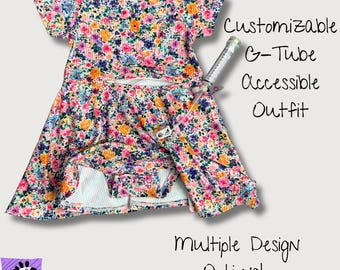 May include: A short-sleeved dress with a vibrant floral pattern in pink, orange, blue, and purple. The dress features a G-tube access opening and includes a medical syringe. Text reads: Customizable G-Tube Accessible Outfit. Multiple Design Options! Love, Wilson.