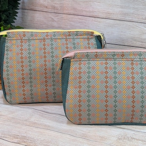 May include: Two rectangular zippered pouches featuring a woven pattern of vertical stripes in muted orange, yellow, and teal on a gray background. The larger pouch has a yellow zipper, while the smaller pouch has a light pink zipper.