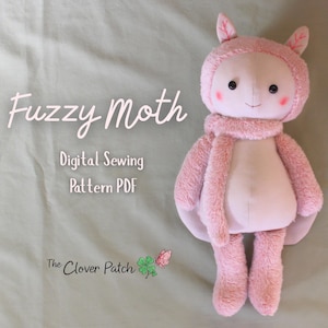 May include: A plush toy shaped like a moth with pink fuzzy fabric, a smooth face, dark eyes, and pink cheeks. The text reads Fuzzy Moth Digital Sewing Pattern PDF and The Clover Patch with a green clover and pink butterfly icon.