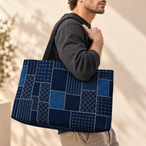 May include: A large rectangular tote bag featuring a patchwork design of various shades of blue fabric. The surface displays a mix of solid navy and denim blue panels alongside sections with white geometric stitching patterns and small cross motifs.