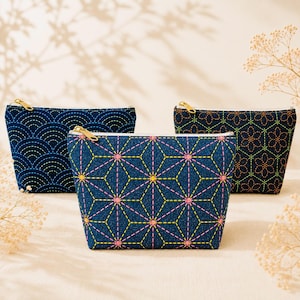 Peut inclure: Trois pochettes zippées bleu foncé ornées de broderies géométriques colorées et complexes. La pochette avant présente un motif d'étoiles jaune et rose, tandis que les pochettes arrière arborent des motifs de vagues et de fleurs avec des fermetures dorées.