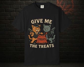 May include: Black t-shirt with a graphic featuring two cartoon cats holding guns, with the text "GIVE ME THE TREATS." One cat is orange and wearing a fedora and pinstripe suit, the other is gray and wearing a leather jacket.