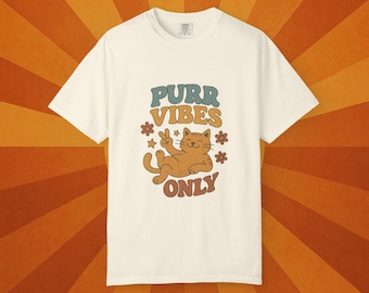 May include: Cream-colored t-shirt with the text "Purr Vibes Only" in retro font. A cartoon cat with a peace sign is in the center, surrounded by flowers. The shirt has a classic crew neck and short sleeves.