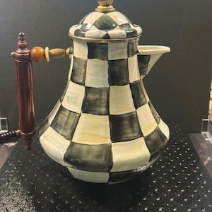 May include: A decorative ceramic teapot with a black and white checkered pattern. The teapot has a dark wooden handle and a gold-colored finial on the lid. The spout is white, and the overall design is ornate and elegant.