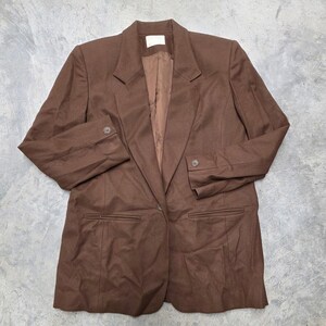 May include: A brown blazer with a single-button closure, two front pockets, and buttoned cuffs. The blazer has a notched lapel and a tailored fit. The interior lining is a lighter shade of brown.