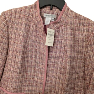 May include: A pink and beige tweed jacket with a stand-up collar and a pink trim. The jacket has a tag that reads "Coldwater Creek" and "14P". The jacket is hanging on a black hanger.