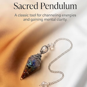 May include: A pointed pendulum featuring a silver-toned metal cap with intricate filigree detailing, attached to a silver chain with clear beads. The pendulum contains multi-colored stone chips. Text reads: Sacred Pendulum. A classic tool for channeling energies and gaining mental clarity.
