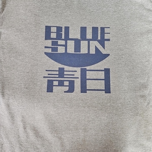 May include: A gray t-shirt with a navy blue graphic. The graphic features the words "BLUE SUN" above Japanese characters. The shirt is made of a soft material and has a crew neck.