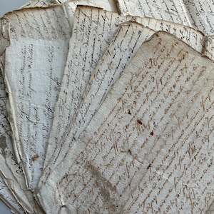May include: A collection of aged, handwritten documents with faded ink. The papers have a textured, off-white appearance with visible wear and tear. The script is in a flowing, cursive style, suggesting historical significance. Some pages show red ink.