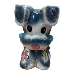 May include: A white ceramic mug with a black handle and the text "But First, Coffee" in a bold, black font. The mug is set against a blurred background, suggesting a cozy setting.