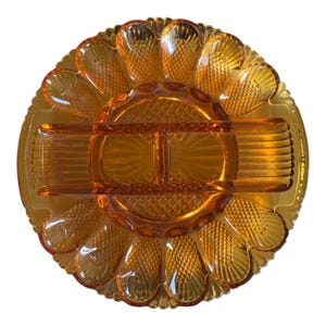 May include: An amber-coloured glass serving dish with multiple compartments. The dish is round with a scalloped edge and a central section divided into two parts. The outer rim features petal-shaped sections, and the dish has a textured, diamond-like pattern.