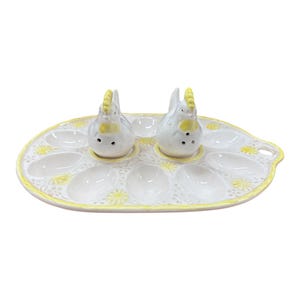 May include: A white ceramic devilled egg serving platter with a yellow trim and floral accents. Two chicken-shaped salt and pepper shakers sit on the platter. The platter has 12 egg indentations.
