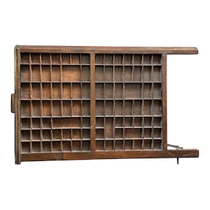 Puede incluir: Una bandeja de imprenta de madera vintage con numerosos compartimentos cuadrados pequeños. La bandeja es de madera marrón oscuro y tiene forma rectangular con un asa lateral. Está diseñada para guardar letras individuales u objetos pequeños.