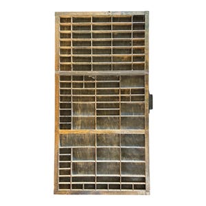 May include: A rectangular wooden printer's type drawer featuring a grid of numerous small, varied compartments. The wood has a dark brown, weathered finish with visible grain patterns and a metal handle attached to the right side of the frame.