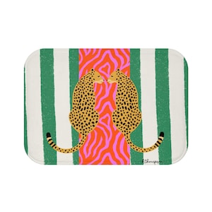 May include: A rectangular bath mat with rounded corners. The mat features a design of two cheetahs facing each other, set against a background of green and white stripes and a central orange and pink zebra print.