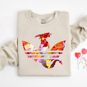 May include: Beige sweatshirt featuring a floral dragon design. The dragon is composed of colorful flowers in red, orange, yellow, and purple. Two heart-shaped lollipops and candies are on the right.
