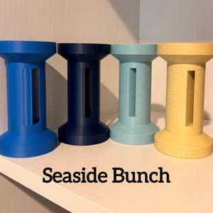 May include: Four colorful, cylindrical decorative objects with a rectangular cutout. The objects are in shades of blue, navy, teal, and tan. The text "Seaside Bunch" is printed in black at the bottom of the image.