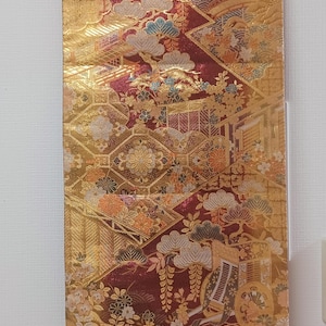 May include: A decorative wall hanging with a traditional Japanese design. The fabric features a gold background with intricate patterns in red, orange, and blue. The hanging is suspended from a wooden rod with a natural cord.